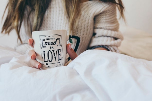 Crop woman with mug on bed