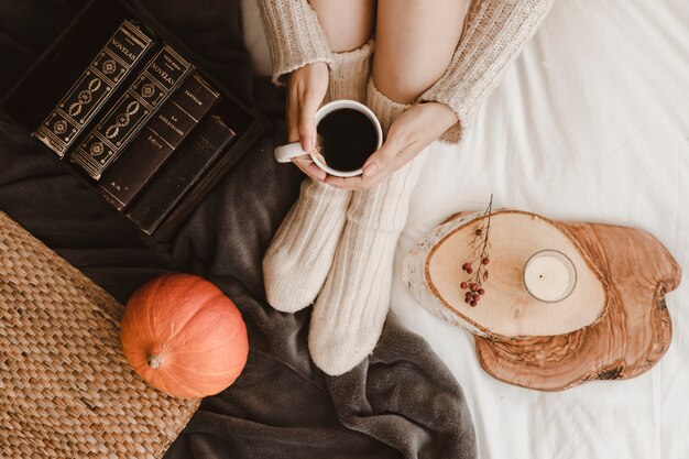 Crop woman with tea near pumpkin and books