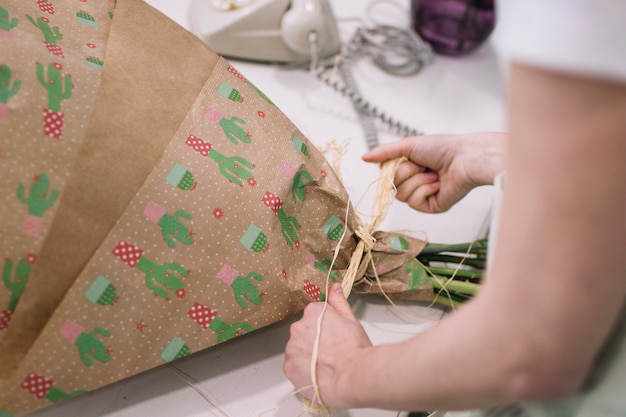 Free photo crop woman wrapping bouquet in paper