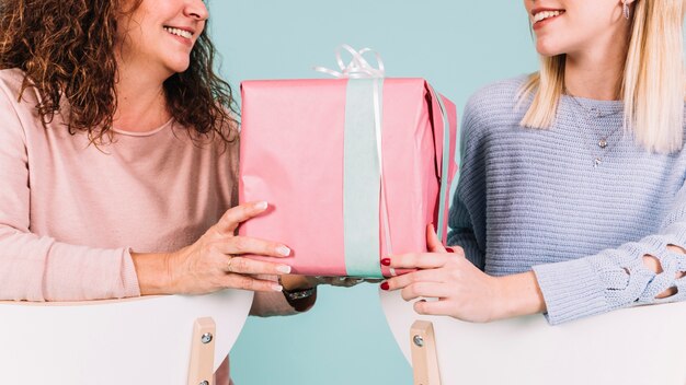 Crop women with gift box on chairs