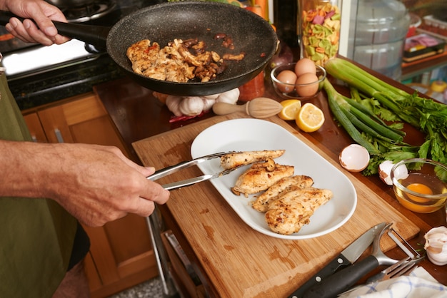 Free photo cropped hands of anonymous cook transferring fried meat with tongs