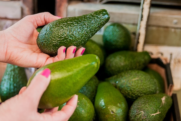 Free photo cropped image of a customer choosing avocados in the supermarket. close up of woman hand holding avocado in market. sale, shopping, food, consumerism and people concept