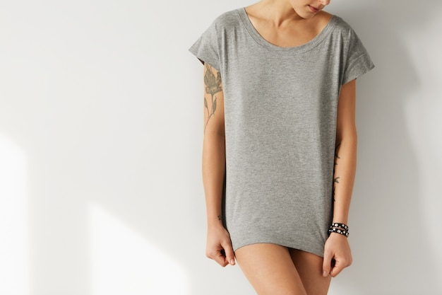 Cropped image of female hipster with perfect body wearing grey oversize T-shirt, posing as model for fashion collection