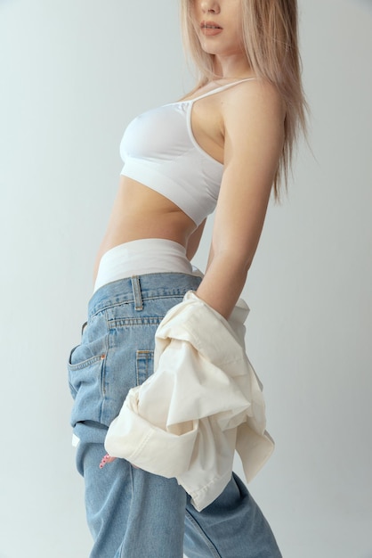 Free photo cropped image of stylish young woman posing in jeans and underwear isolated over grey studio background