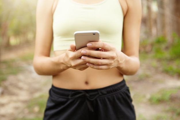 Cropped image of woman training outdoors and tracking her fitness route on cell phone.