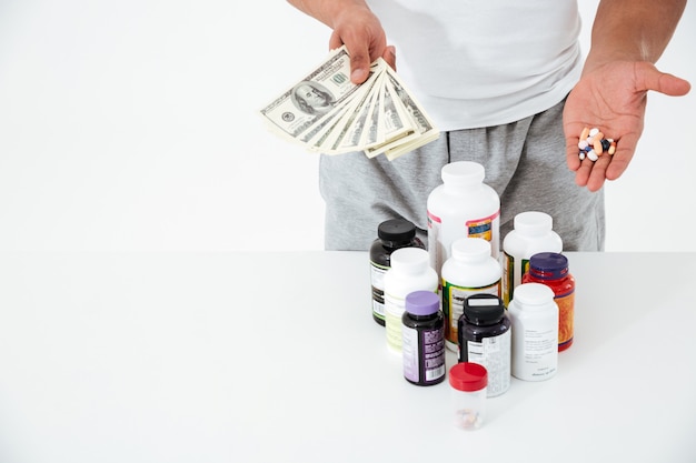 Cropped image of young sportsman holding vitamins and money.