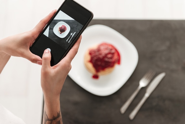 Free photo cropped photo of woman make photo of pancakes by phone.