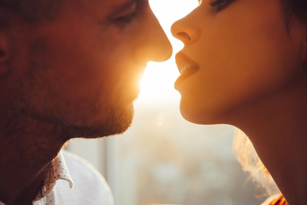 Cropped photo of young lovers kissing near window at home