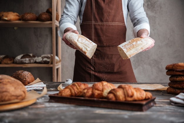 Free photo cropped photo of young man baker holding bread.