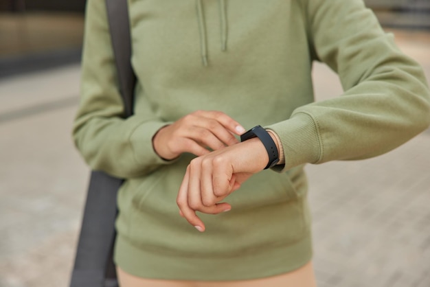 Free Photo cropped shot of unknown woman checks fitness results on smartwatch monitors pulse dressed in casual sweatshirt carries karemat poses outdoors faceless sportswoman uses modern gadget for sport