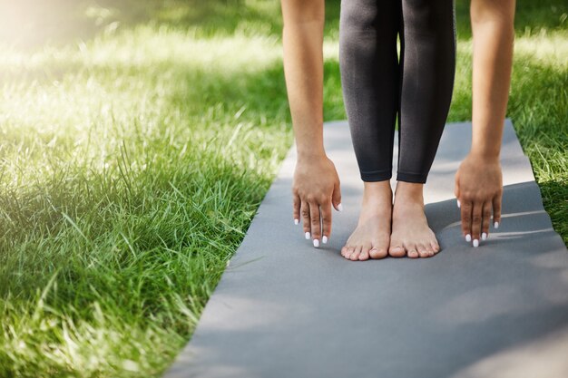 Cropped shot of woman doing pilates or yoga or exercises in park. Hands and feet planted on yoga mat.