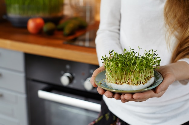 Free photo cropped shot of a woman holding in her hands a saucer with a home grown organic sprout micro greens against cozy kitchen interior. healthy raw food concept. copy space for text. selective focus