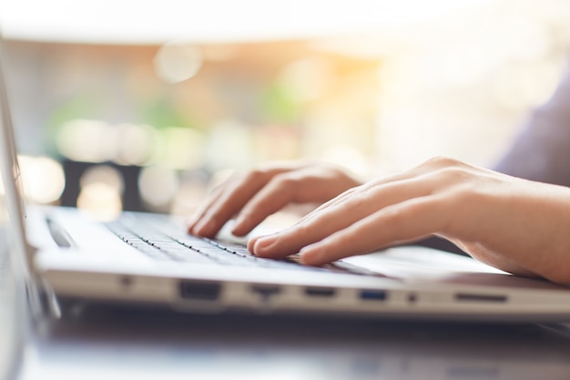 Cropped shot of woman's hands typing on keyboard of her laptop while preparing her diploma paper.