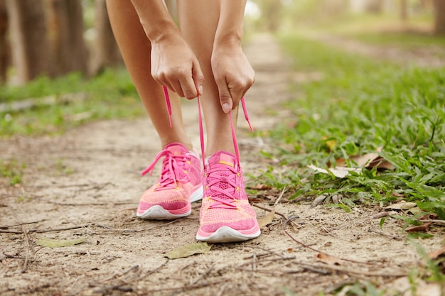 Cropped shot of young woman runner tightening running shoe laces, getting ready for jogging exercise outdoors.