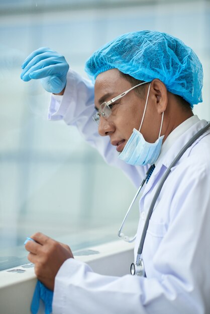 Cropped side view of surgeon tired after the surgery leaning at the window