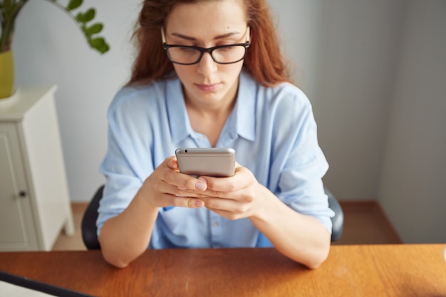 Free Photo cropped view portrait of cute redhead girl texting on the cell phone at the wooden desk