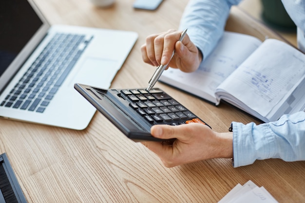 Free photo cropped view of professional serious finance manager, holding calculator in hands, checking company month's profits