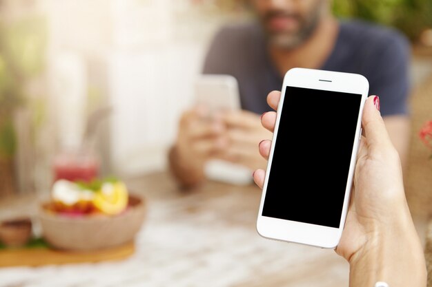 Cropped view of young female using touchscreen smartphone during lunch at cafe