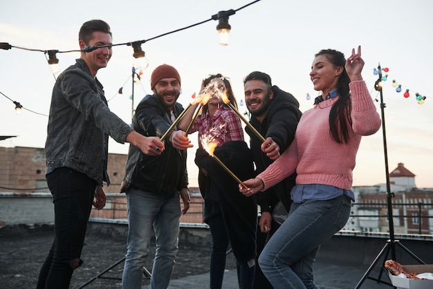 Free Photo cross the flames. playing with sparklers on the rooftop. group of young beautiful friends