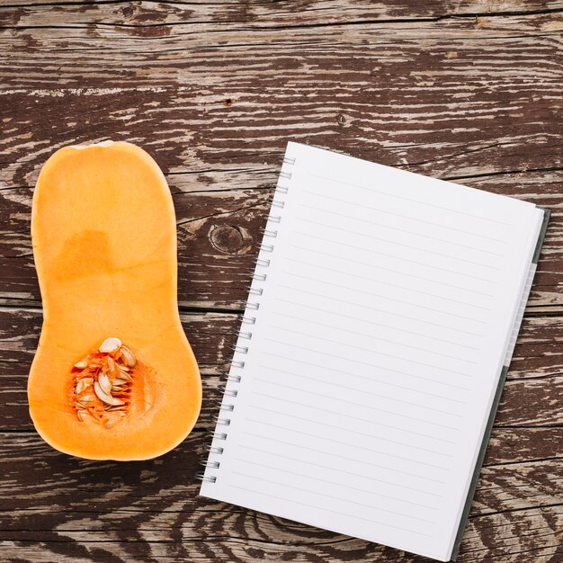 Cross section of butternut squash and spiral notepad on wooden desk