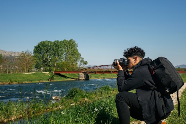 Free photo crouching young man taking picture of flowing river