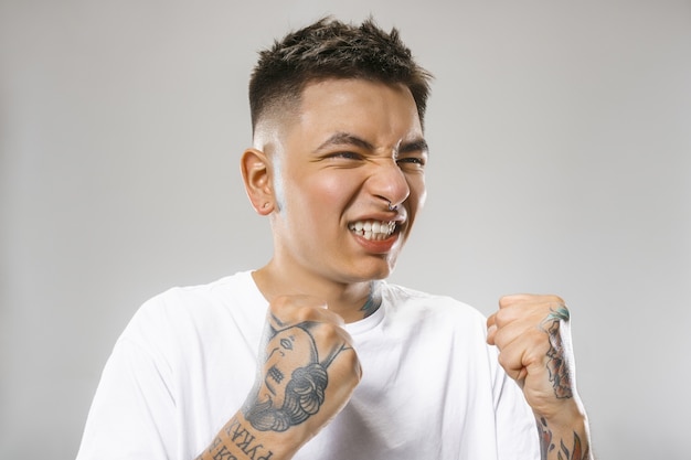 Crying emotional angry man screaming on gray studio background. Emotional, young face. male half-length portrait. Human emotions, facial expression concept.