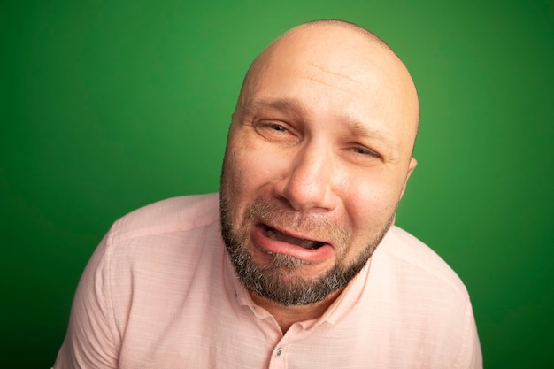 Crying looking straight ahead middle-aged bald man wearing pink t-shirt isolated on green