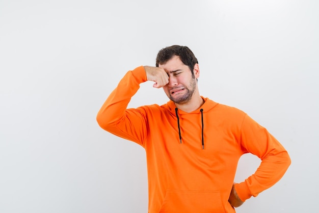 The crying man is holding his hand on eye and putting other on waist  on white background