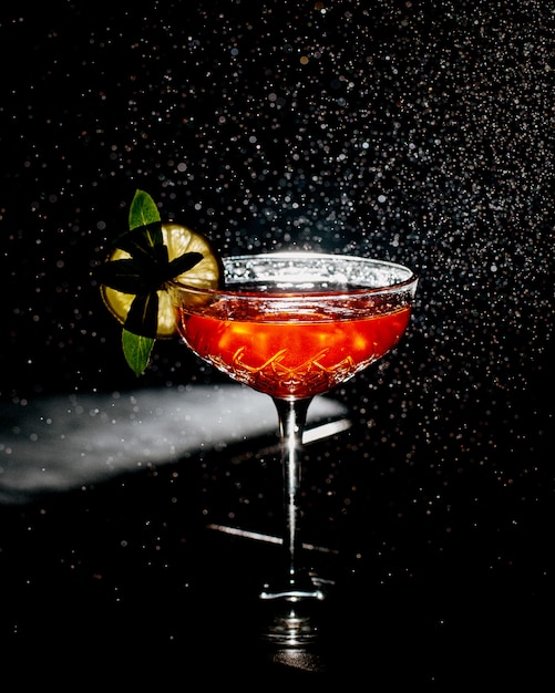 A crystal glass of orange cocktail garnished with lime slice in dark background with light