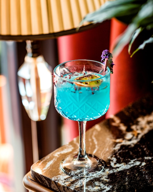 crystal glass with blue cocktail garnished with dried orange slice