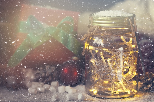 Free photo crystal jar with lights with a gift next to it while it snows