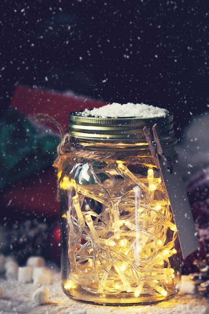 Free photo crystal jar with lights with a gift next to it while it snows