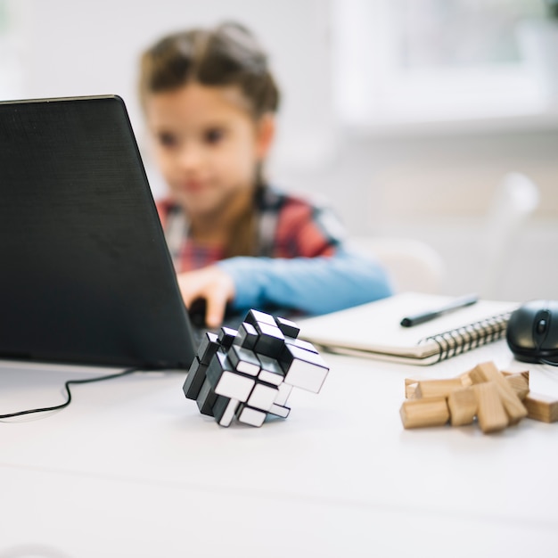 Free photo cube puzzle in front of girl using laptop on white desk