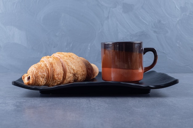 Cup of black coffee and croissant for breakfast on grey background.