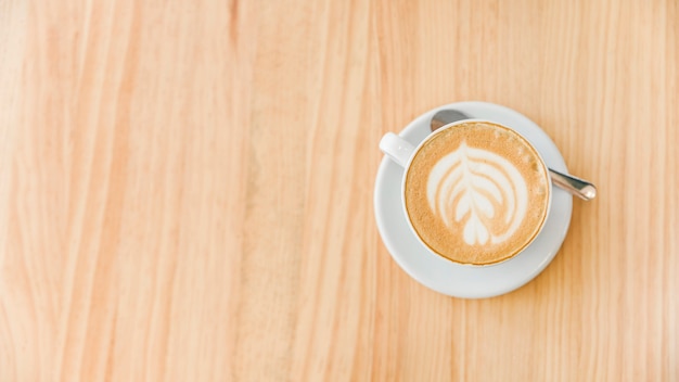 Cup of cappuccino coffee with art latte and spoon on wooden background