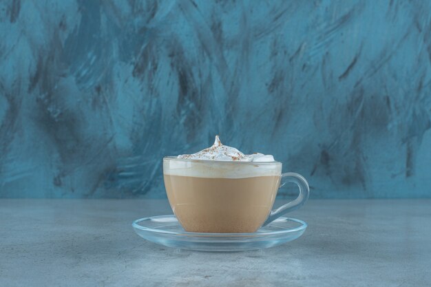 A cup of cappuccino on a saucer , on the blue table. 