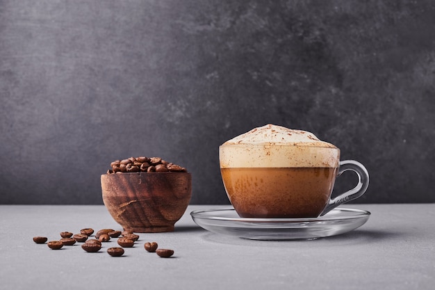 A cup of cappuccino with coffee beans around.