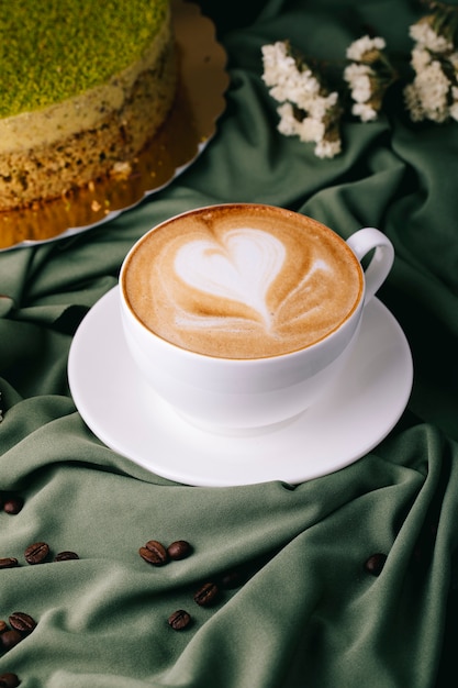 Free Photo cup of cappuccino with coffee beans and cake on the table