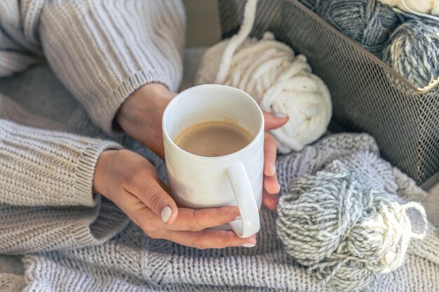 A cup of coffee in female hands and a thread of yarn