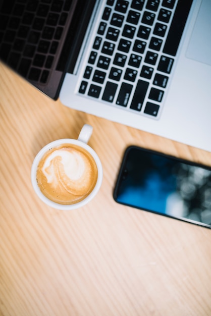 Free photo cup of coffee near mobile phone and laptop at table