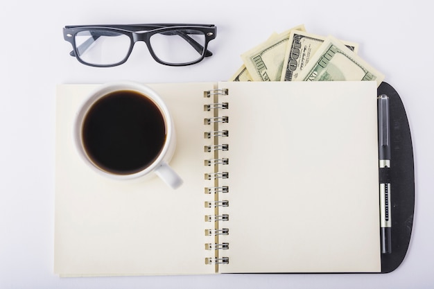 Cup of coffee on notebook with glasses on desk