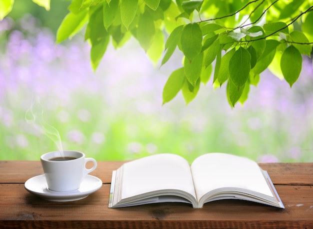 Free photo cup of coffee and open book on wooden table