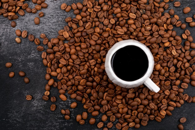 Free Photo cup of coffee surrounded with coffee beans on black surface