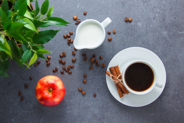 Free photo a cup of coffee with apple, dry cinnamon, plant, milk on gray surface, top view.