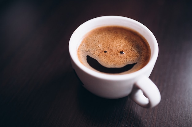 Cup of coffee with foam, smile face, on desk isolated