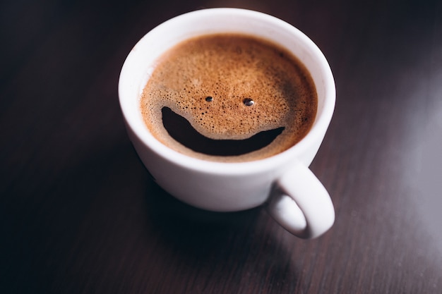 Cup of coffee with foam, smile face, on desk isolated