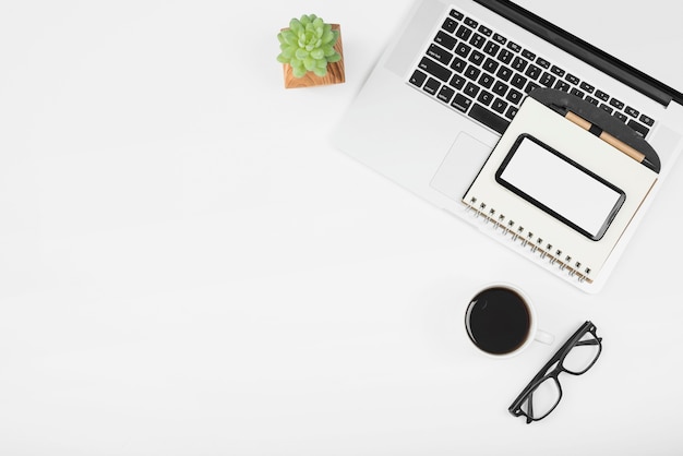 Cup of coffee with laptop; cell phone and diary with pen over white background