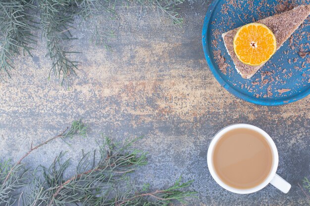 A cup of coffee with piece of tasty cake on blue plate.