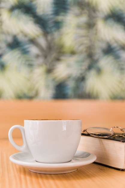 Cup of coffee with spectacles and book on wooden table