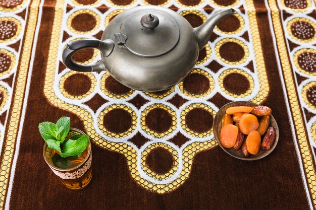 Cup of drink near retro teapot and dried fruits on mat